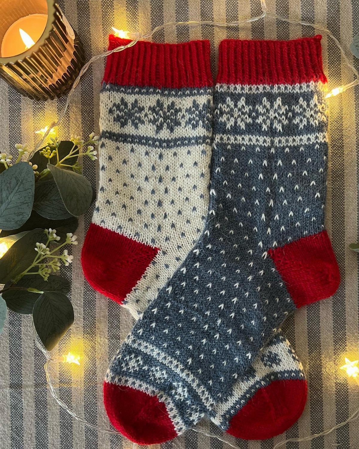 Knitted Fair Isle socks with red accents surrounded by fairy lights and a candle.