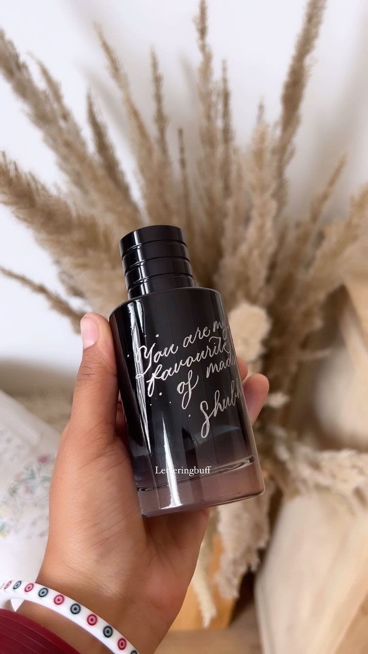 Hand holding a black bottle with white handwritten calligraphy and dried grass background