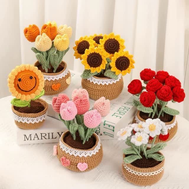 Crocheted colorful flowers in small brown yarn pots arranged on white books.