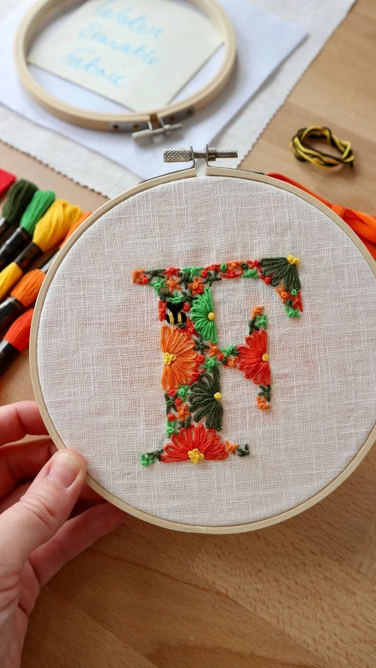 Embroidered letter F with colorful floral patterns in a wooden embroidery hoop