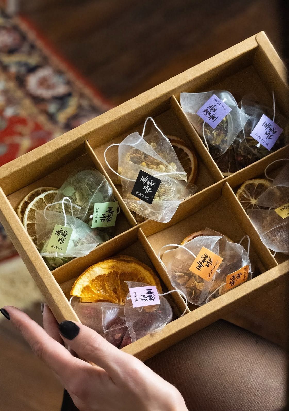 Hand holding a cardboard gift box containing tea bags and dried citrus slices.