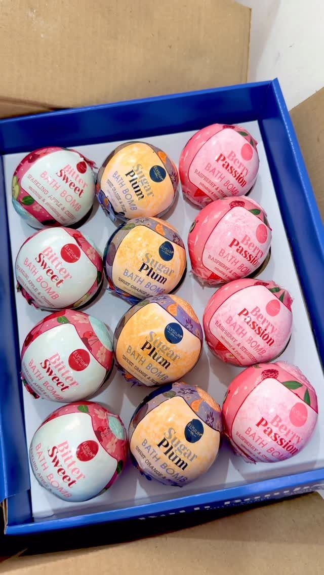 Twelve colorful bath bombs in a blue box with fruity labels.