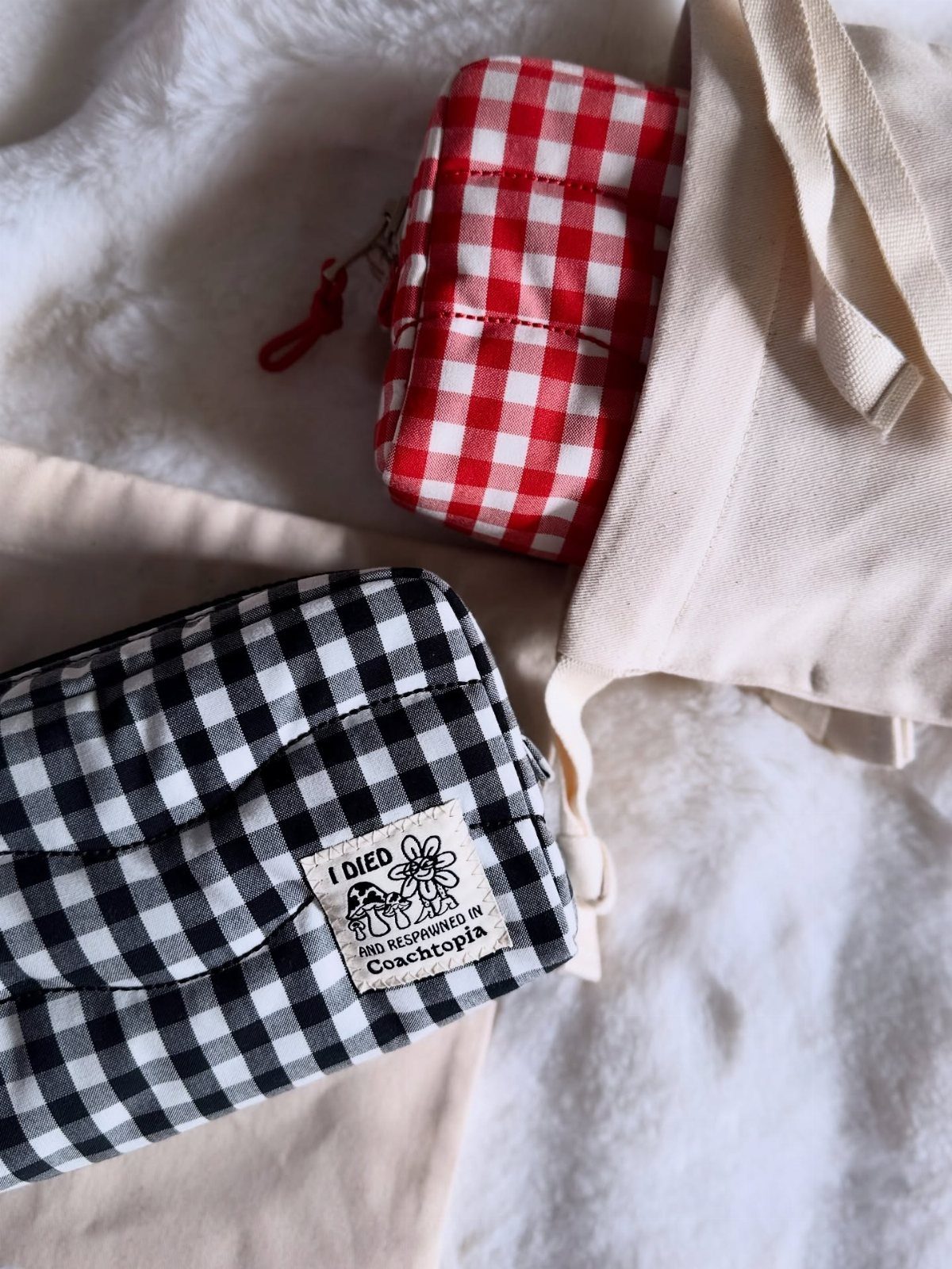 Two gingham patterned pouches and a beige bag on a white fluffy background.