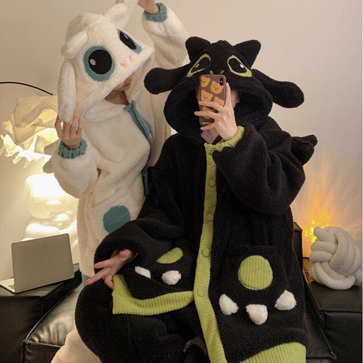 Two people wearing plush animal onesie pajamas in white and black colors.