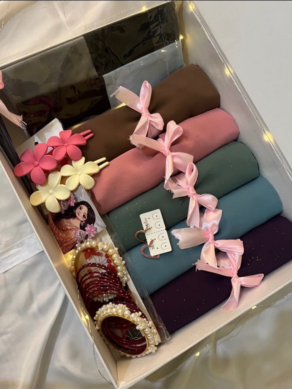 Five colorful rolled scarves tied with pink ribbons in a white gift box.