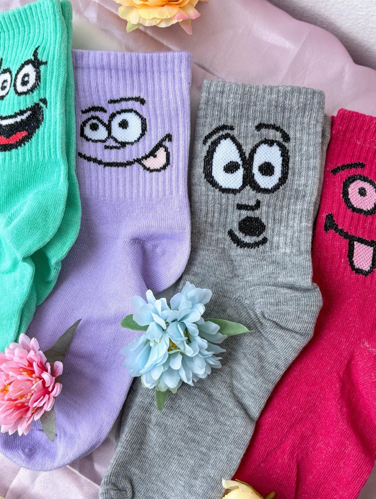 Colorful cartoon face socks in teal, purple, grey, and pink with small flowers.