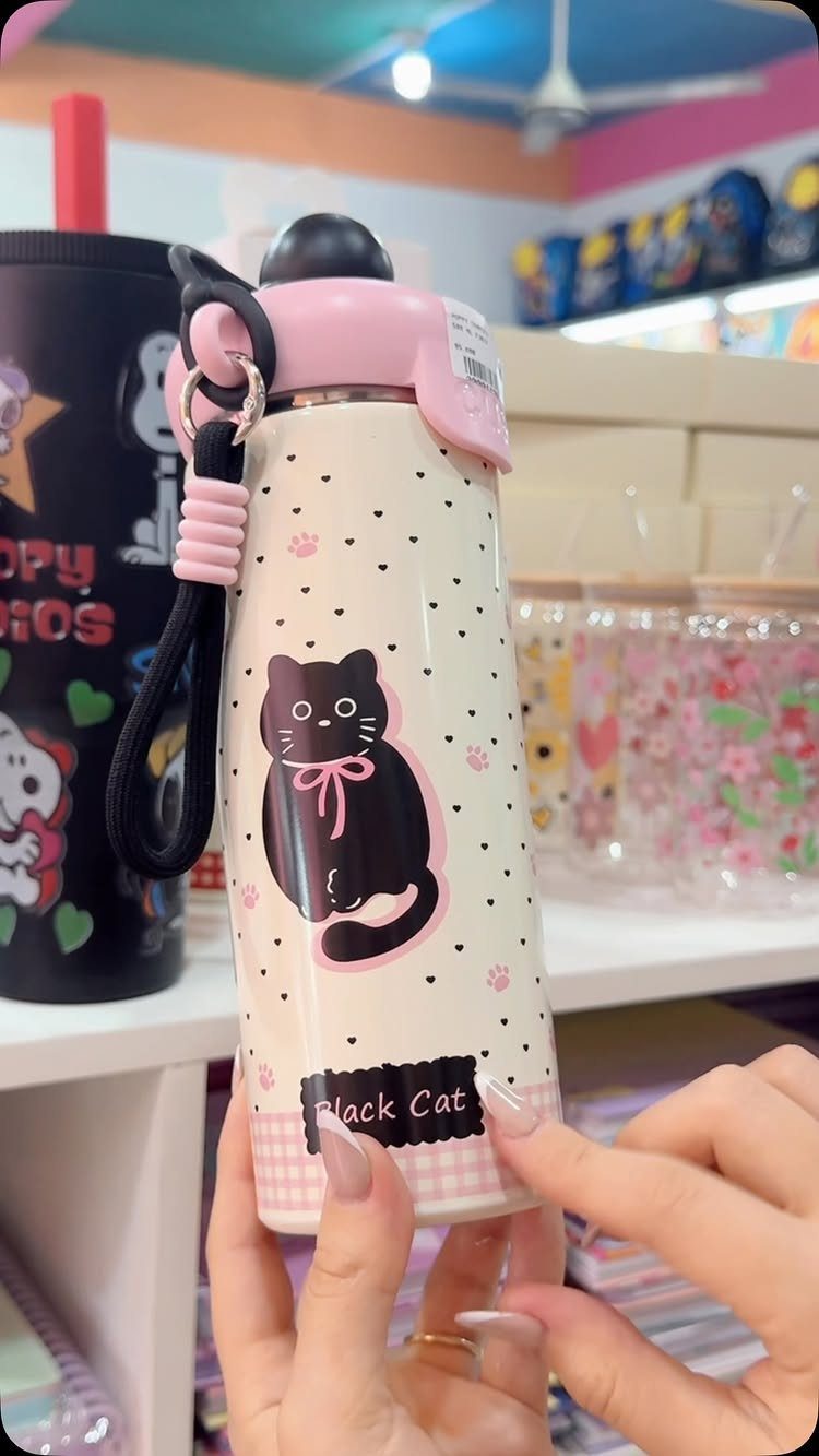 Cream-colored water bottle with a black cat illustration and pink lid held by hands.