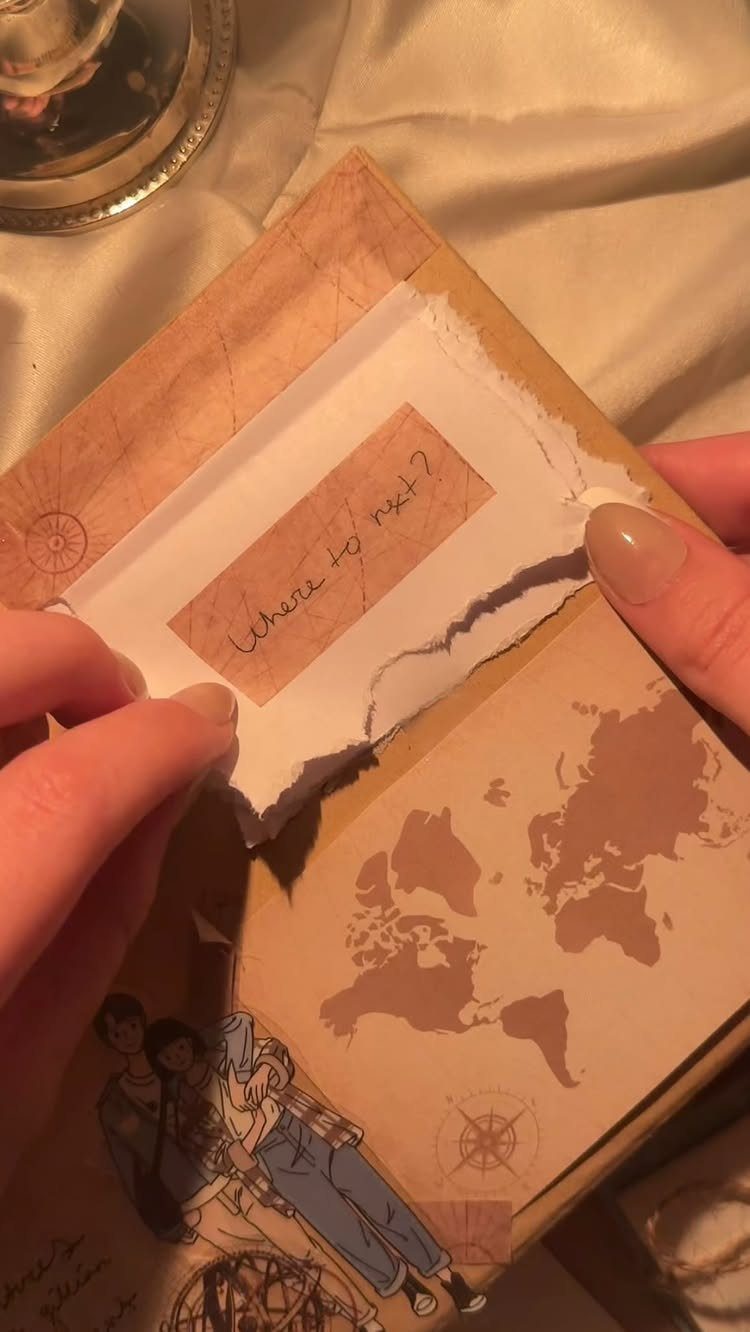 Vintage travel journal with a world map and handwritten note held by hands.