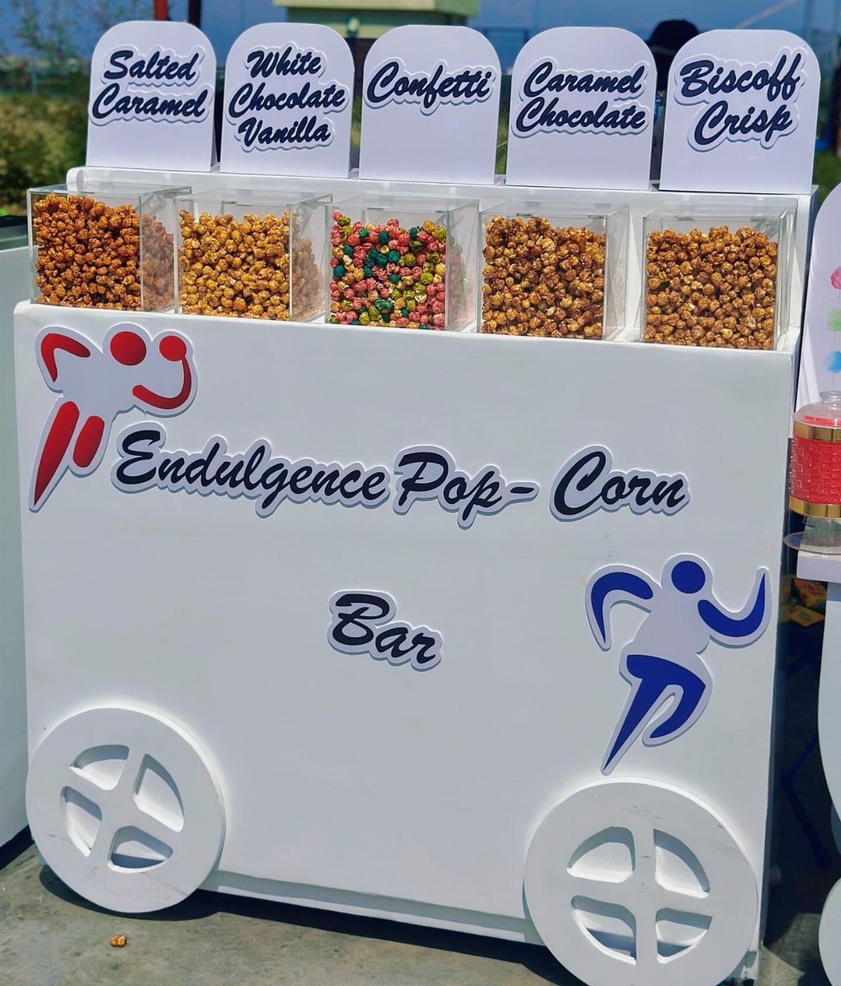 White popcorn bar cart with five bins of gourmet flavored popcorn and labels.