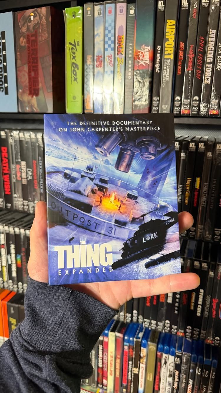Hand holding a movie documentary DVD in front of shelves of movie cases.