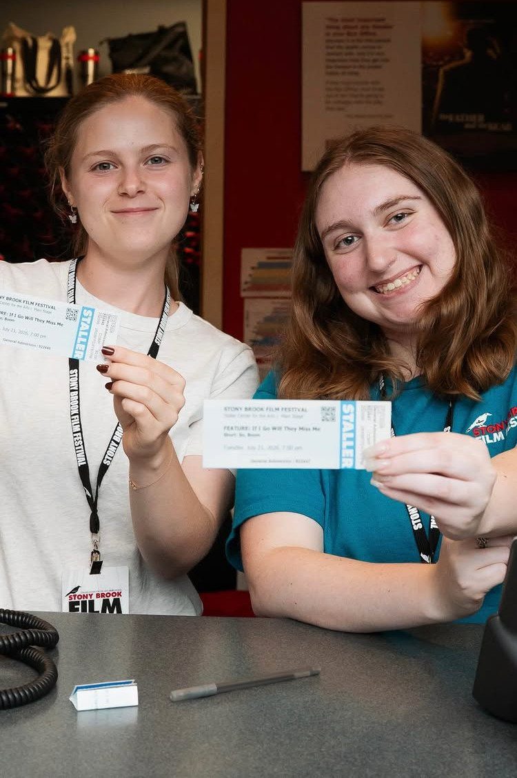 Two women holding white Stony Brook Film Festival tickets and wearing event t-shirts.