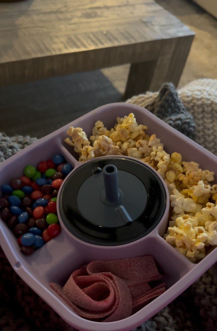 Purple divided snack tray filled with popcorn, candies, and fruit leather on a blanket.