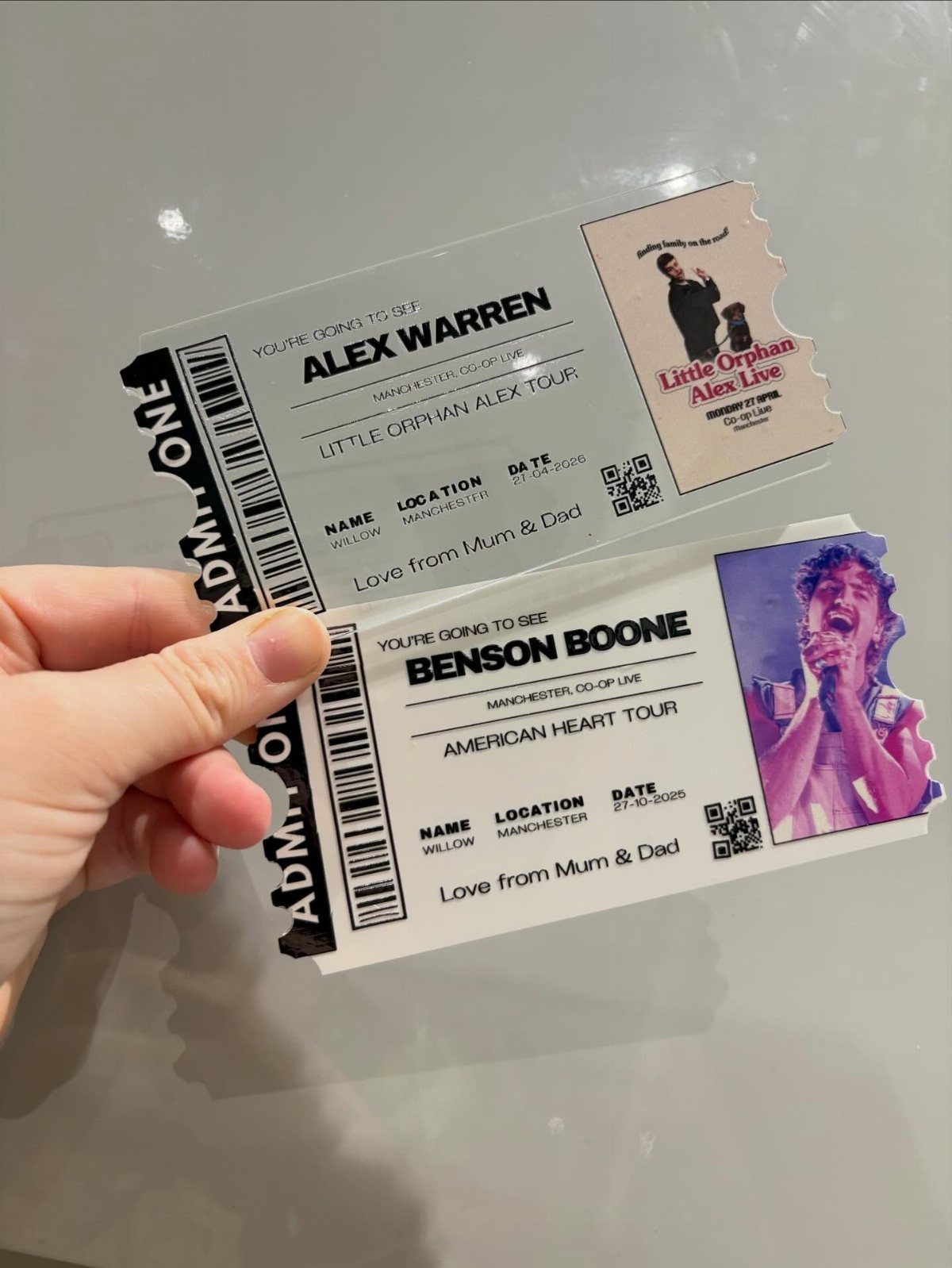 Two printed concert tickets for Alex Warren and Benson Boone held by a hand.
