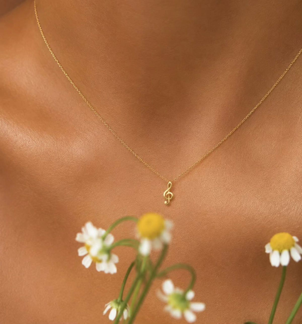 Gold treble clef pendant necklace worn on a person with daisies in foreground