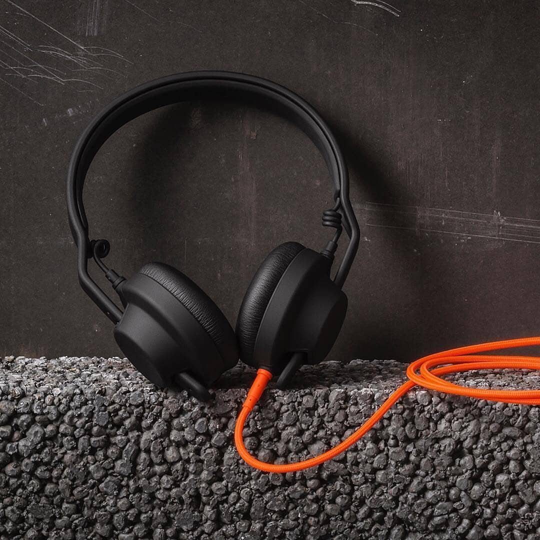 Black over-ear headphones with a bright orange cable on a grey carpet.