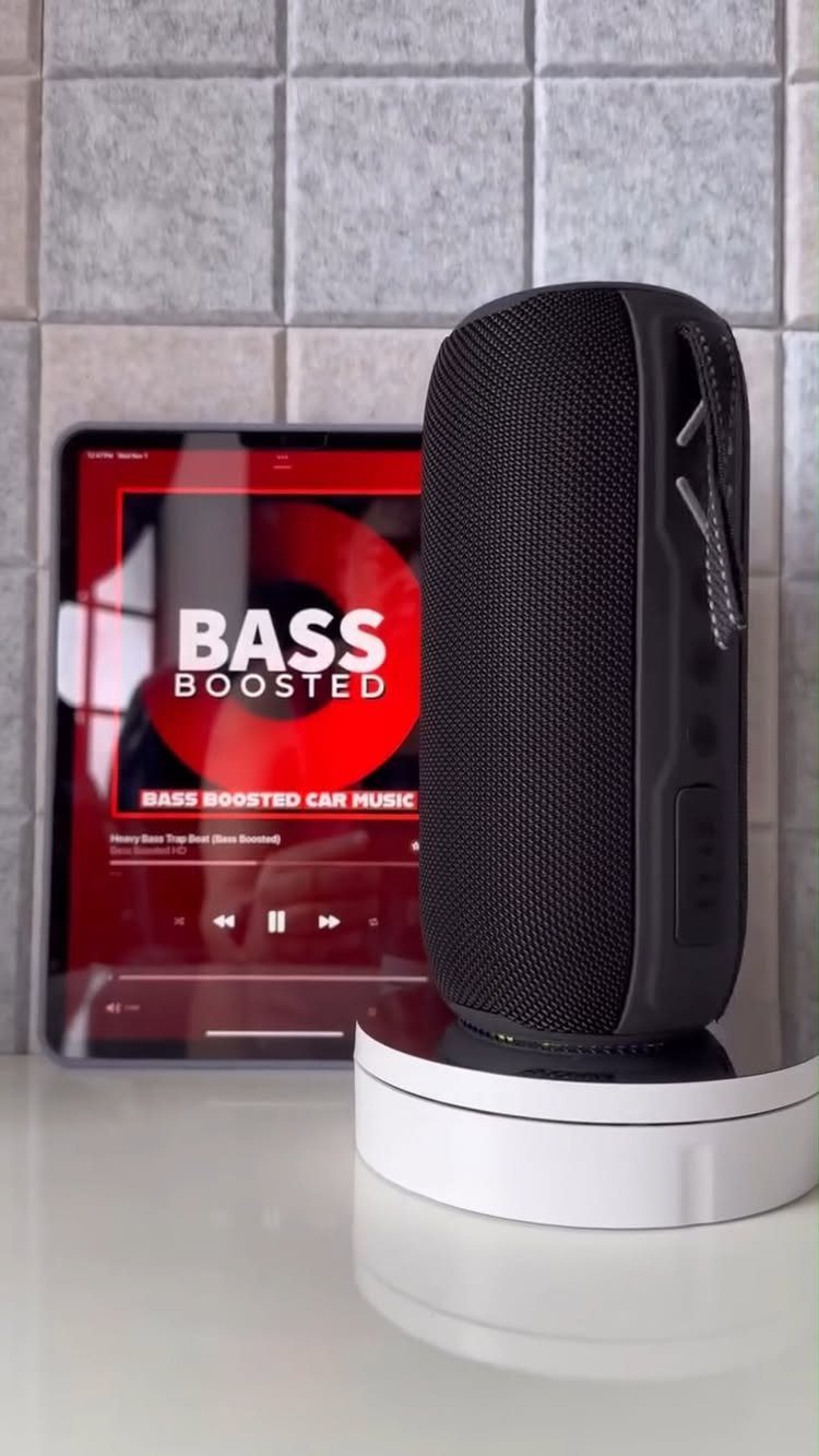 Black portable speaker and tablet displaying bass boosted music on a white surface