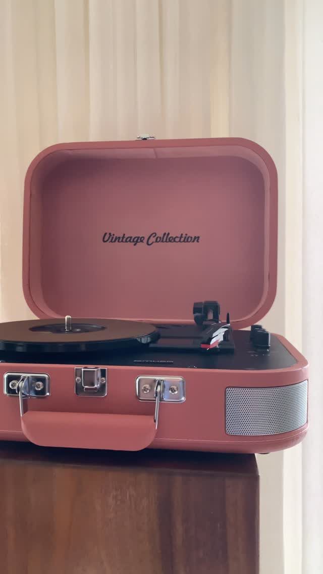 Pink portable suitcase record player with a black vinyl record on a wooden table