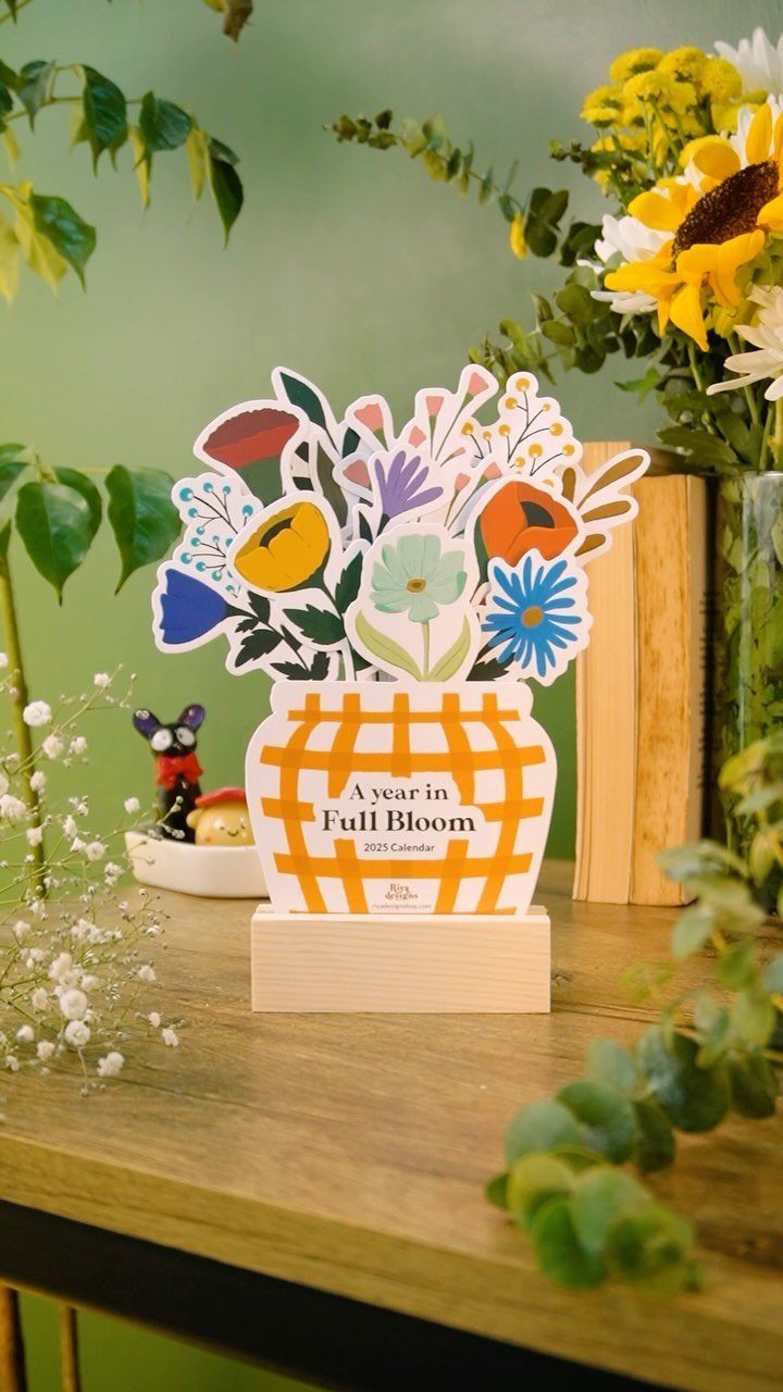 Acrylic flower pot calendar with colorful floral illustrations on a wooden table.