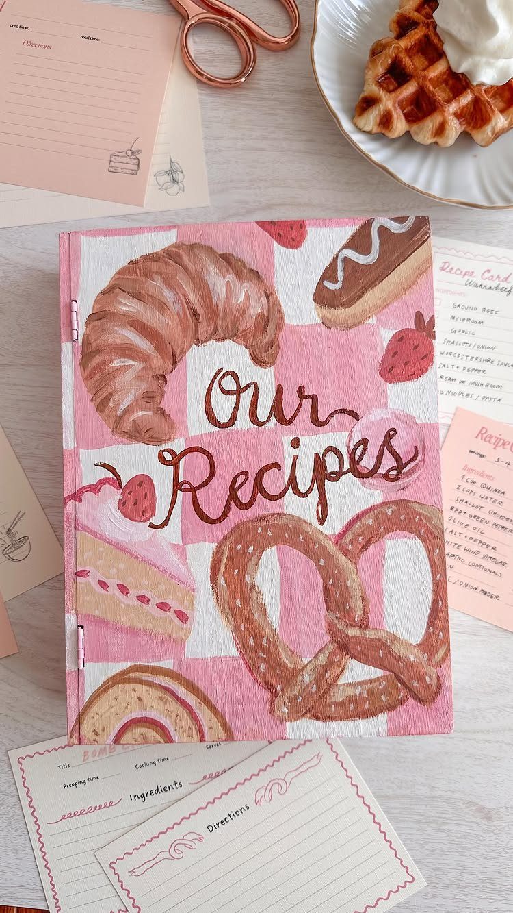 Pink checkered cookbook titled Our Recipes surrounded by recipe cards and a waffle.
