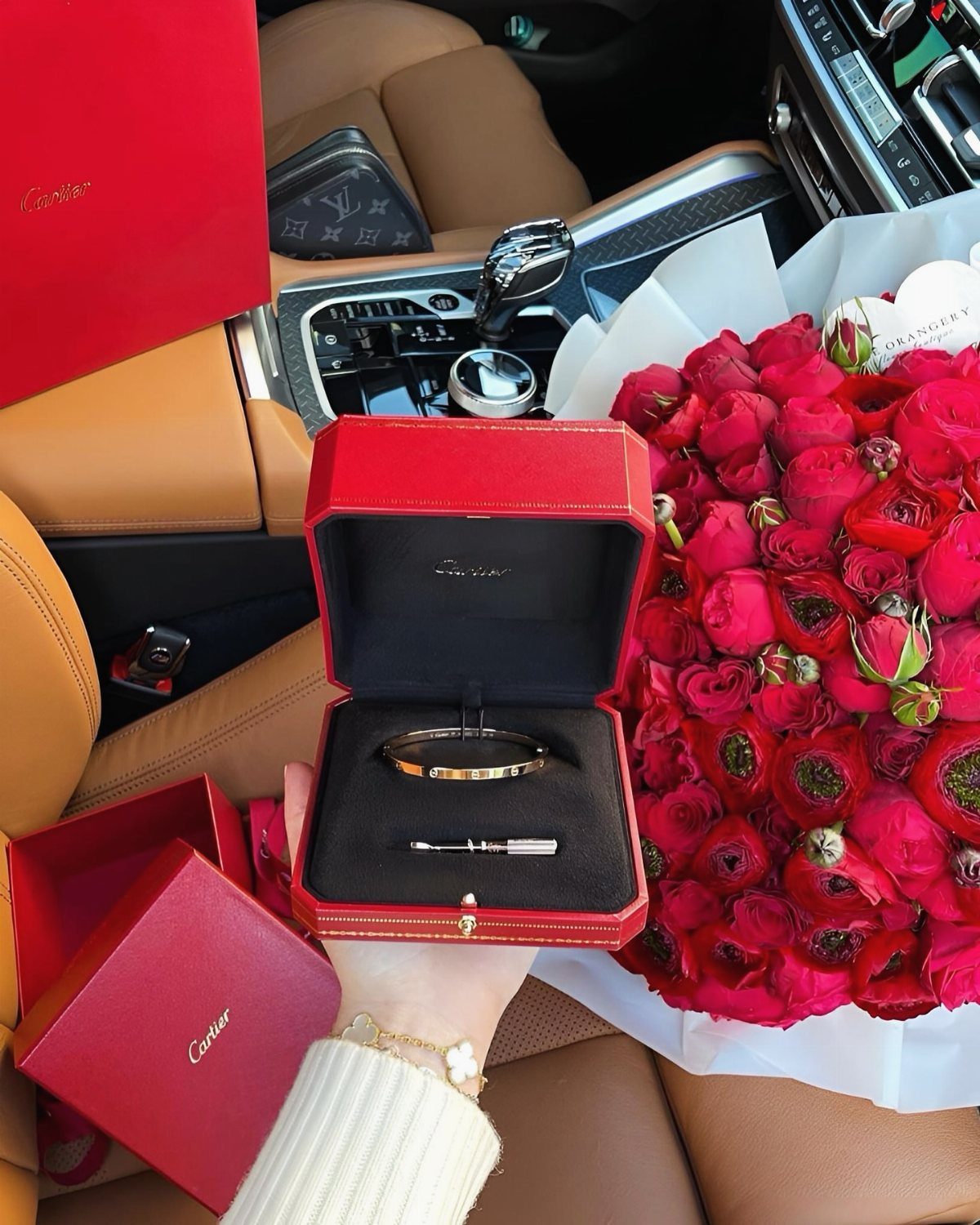 Gold bracelet and ring in a red box next to red roses.