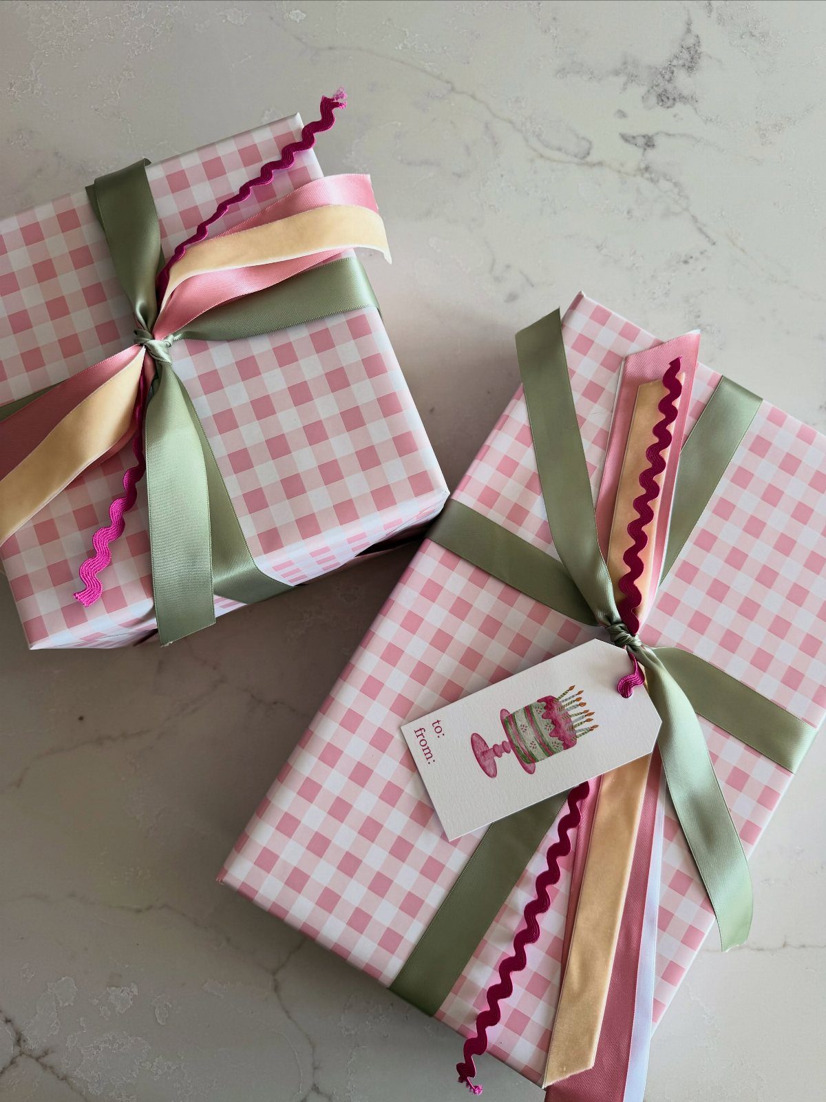 Two gifts wrapped in pink gingham paper with multi-colored ribbons on marble.
