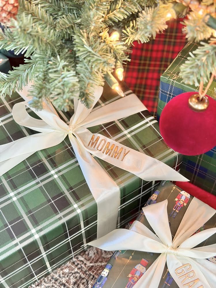 Wrapped gifts with personalized name ribbons under a lit Christmas tree