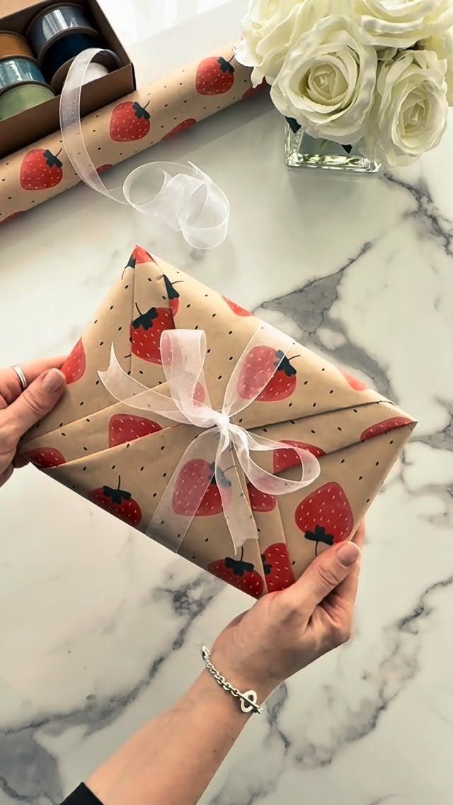 Wrapped gift box with strawberry pattern paper and white ribbon on marble surface
