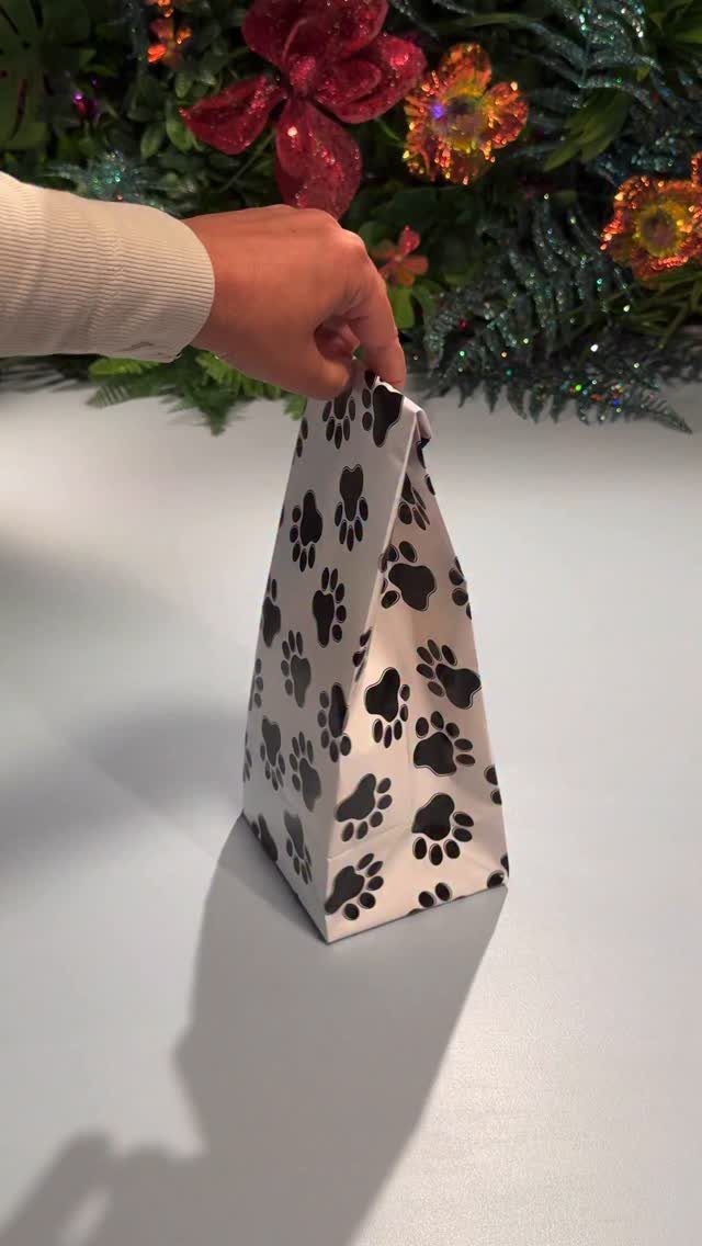 White gift bag with black paw print seamless pattern held by a hand.