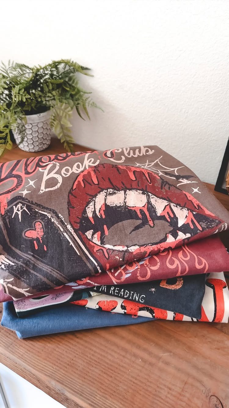 Stacked fabric book sleeves on a wooden table with a small potted plant.