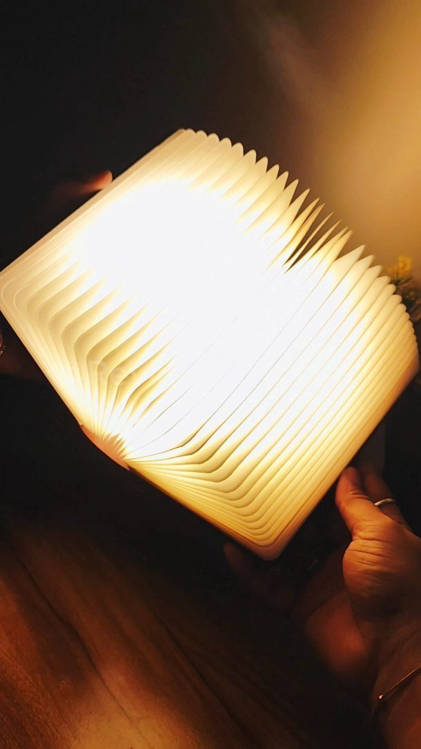Glowing book-shaped lamp held by hands in a dark, warm setting