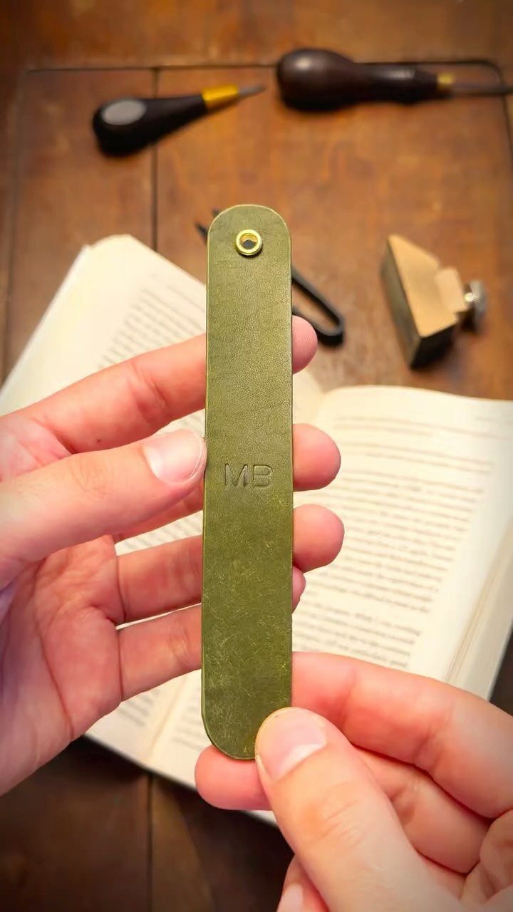 Olive-green leather bookmark with stamped initials held over an open book.