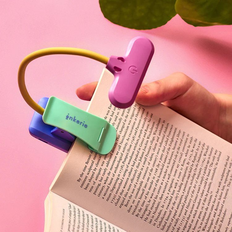 Colorful clip-on reading light attached to an open book held by a hand.