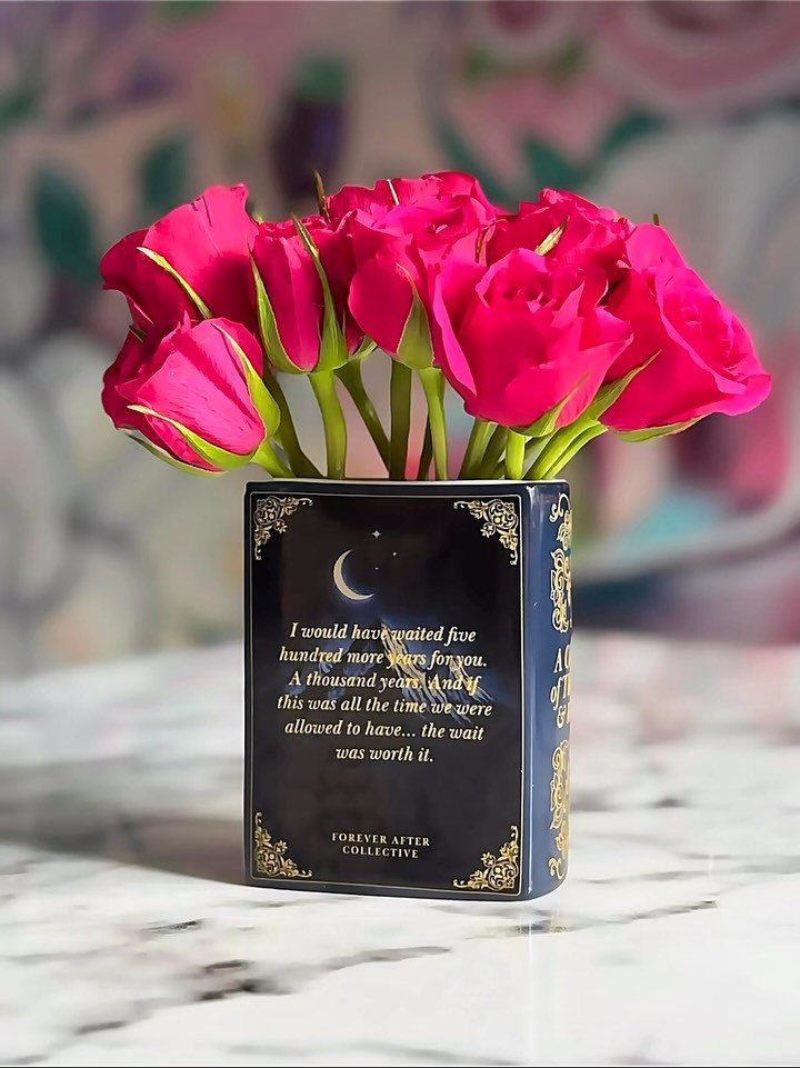 Book-shaped dark blue vase with gold accents holding a bouquet of pink roses.