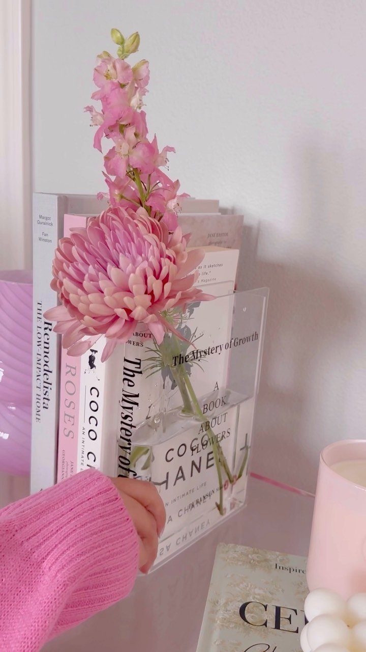 Books in a clear acrylic holder with a pink flower and pink sweater.
