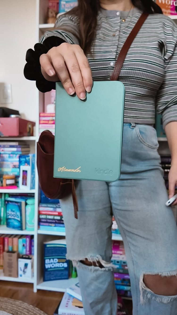 Person holding a teal Kindle e-reader case in front of a bookshelf
