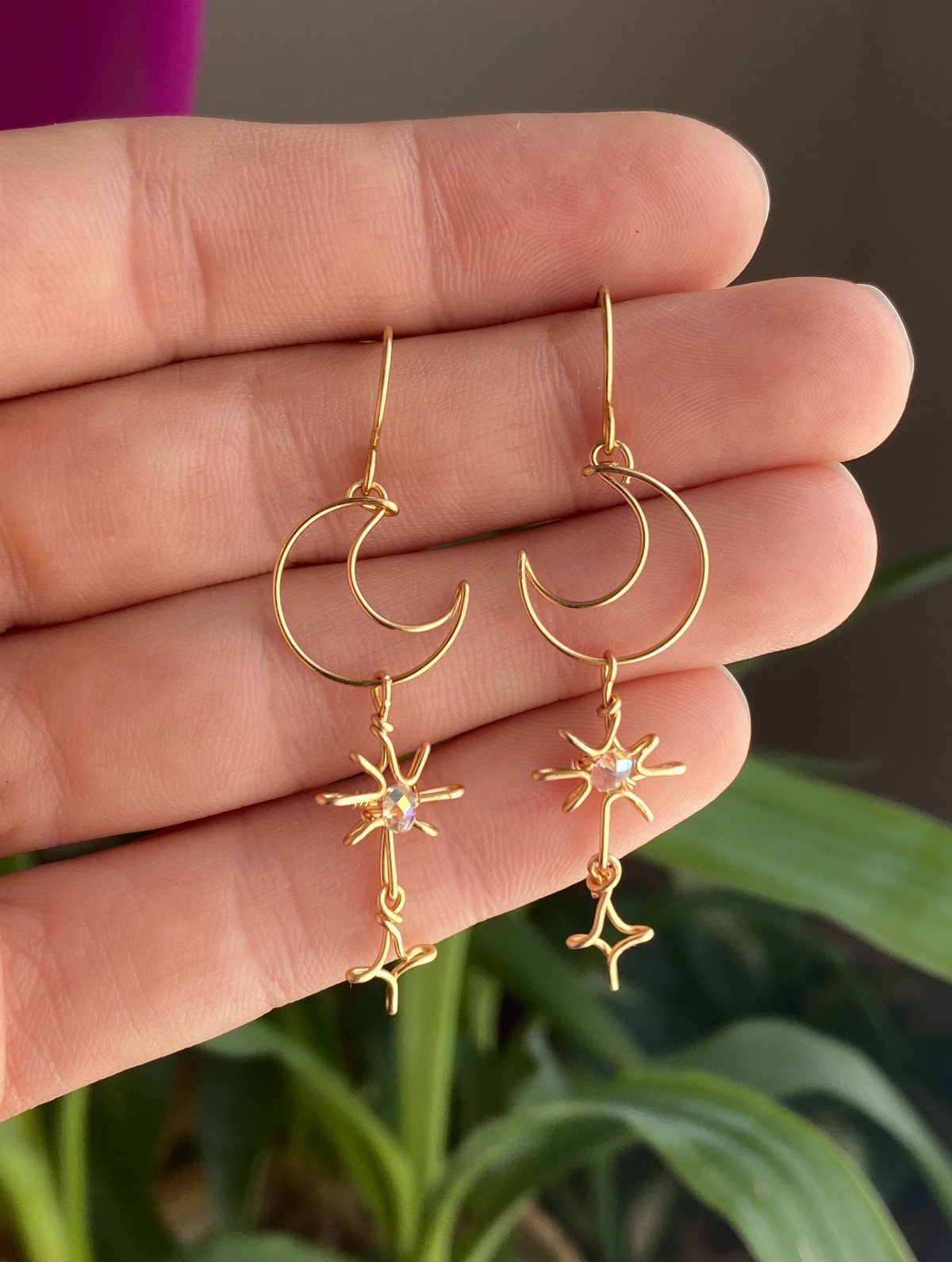 Gold crescent moon and star earrings held in a person's hand