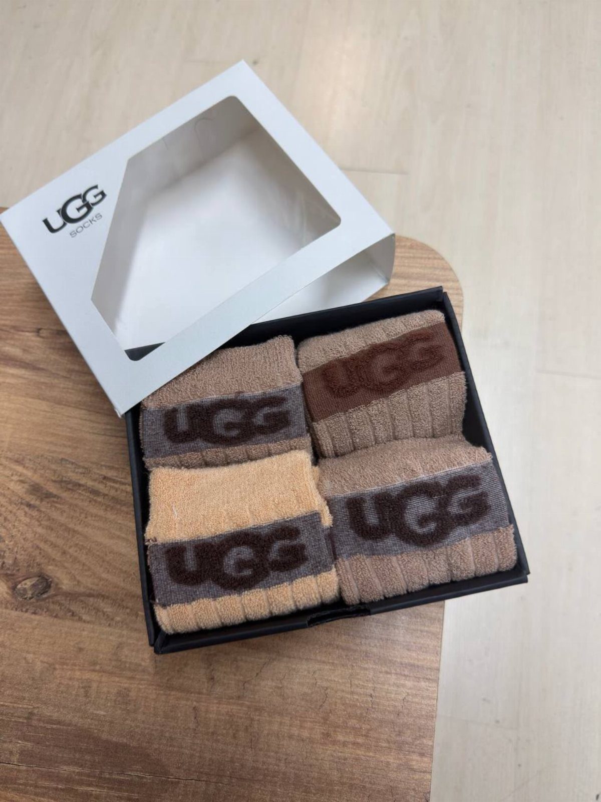 Four pairs of neutral toned UGG socks folded in a black gift box.