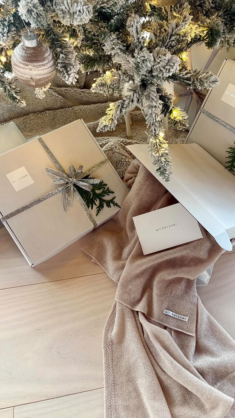 White gift box and beige knit scarf under a frosted Christmas tree.