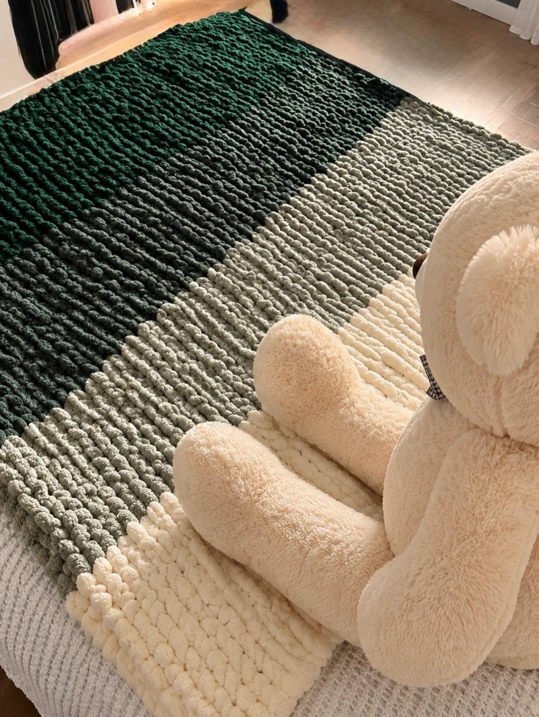 Chunky knit striped throw blanket in green and cream with a teddy bear.