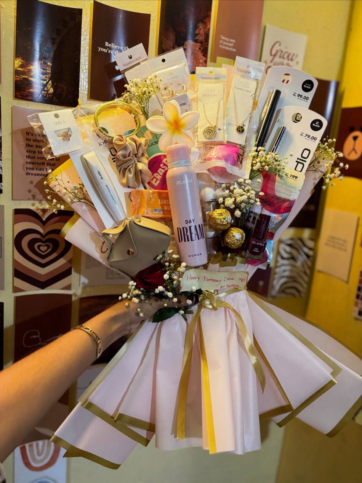 Gift bouquet with skincare, jewelry, and flowers wrapped in pink and gold paper.