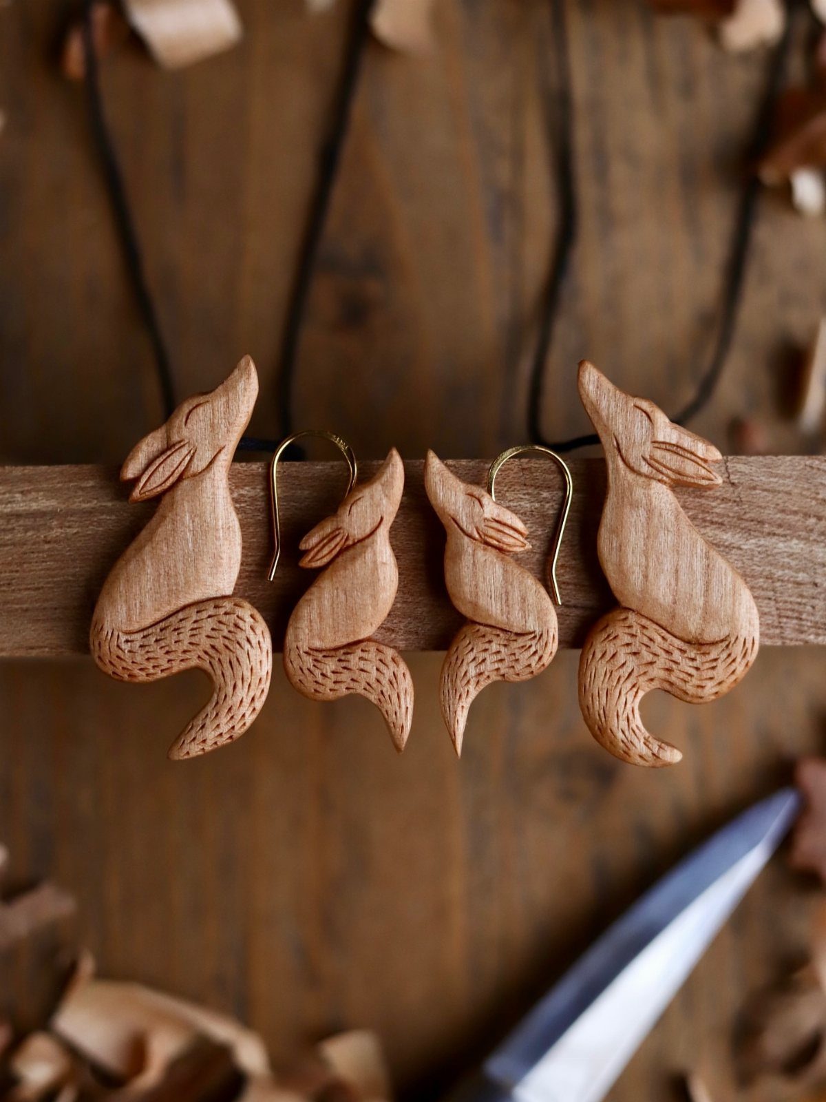 Hand-carved wooden fox pendants and earrings resting on a rustic wooden beam.
