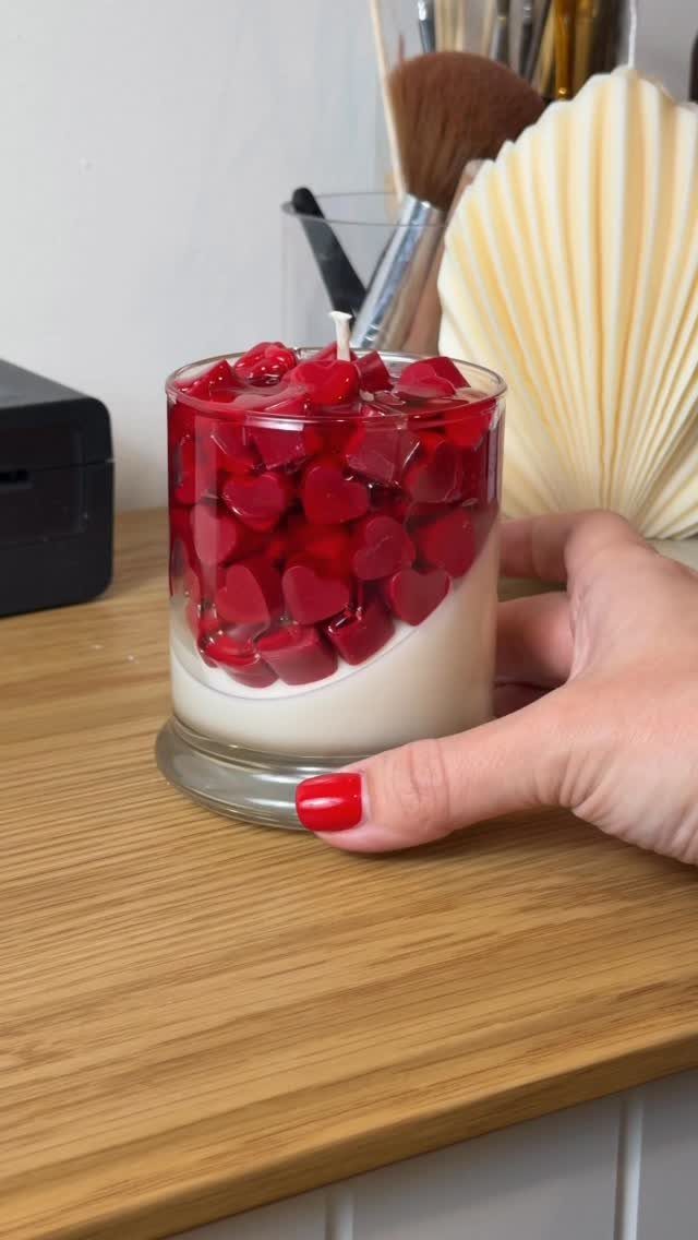 Heart-shaped red and white candle in a glass jar held by a hand.