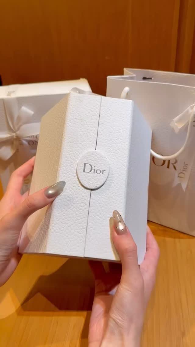 Hands holding a white textured Dior gift box with a shopping bag behind.