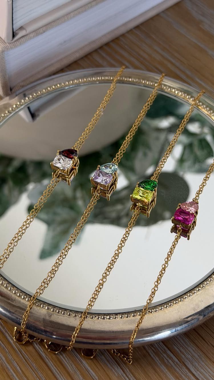 Four gold heart-shaped gemstone necklaces resting on a circular mirror tray.