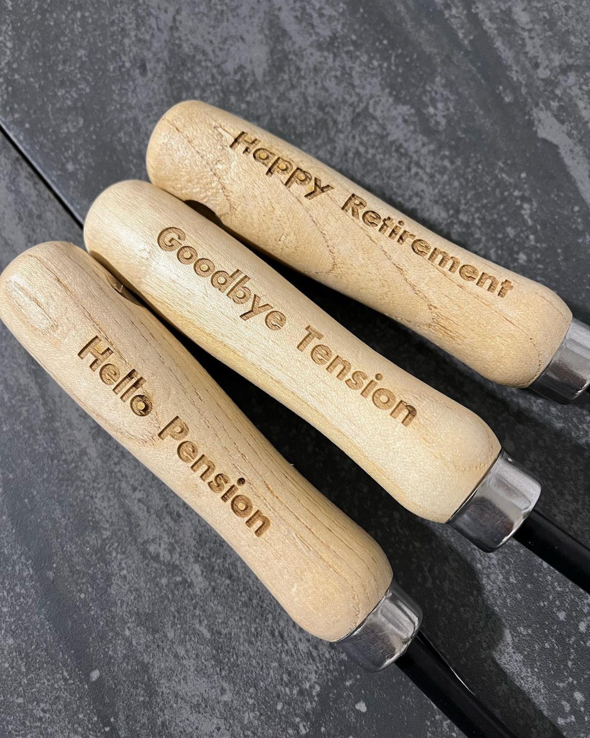 Engraved wooden handles of gardening tools with retirement messages on a dark background