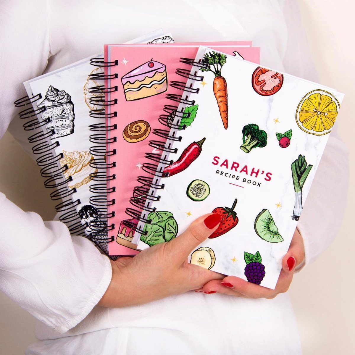 Person holding a personalized recipe book with colorful vegetable illustrations on the cover.