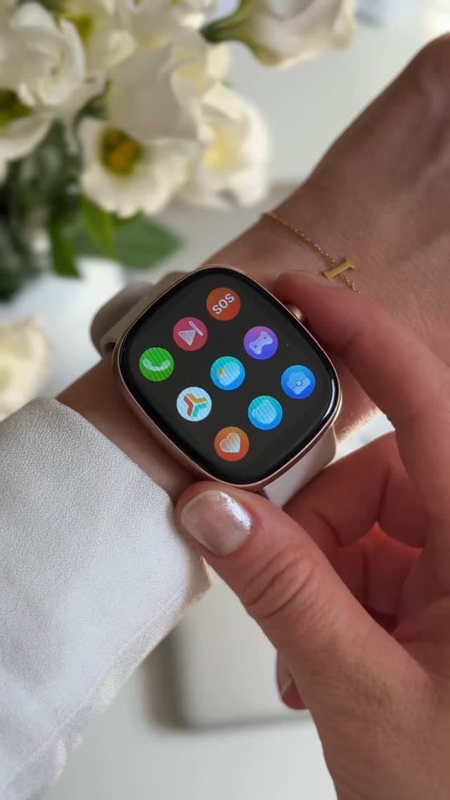 Gold-toned smartwatch on a woman's wrist with white flowers in the background