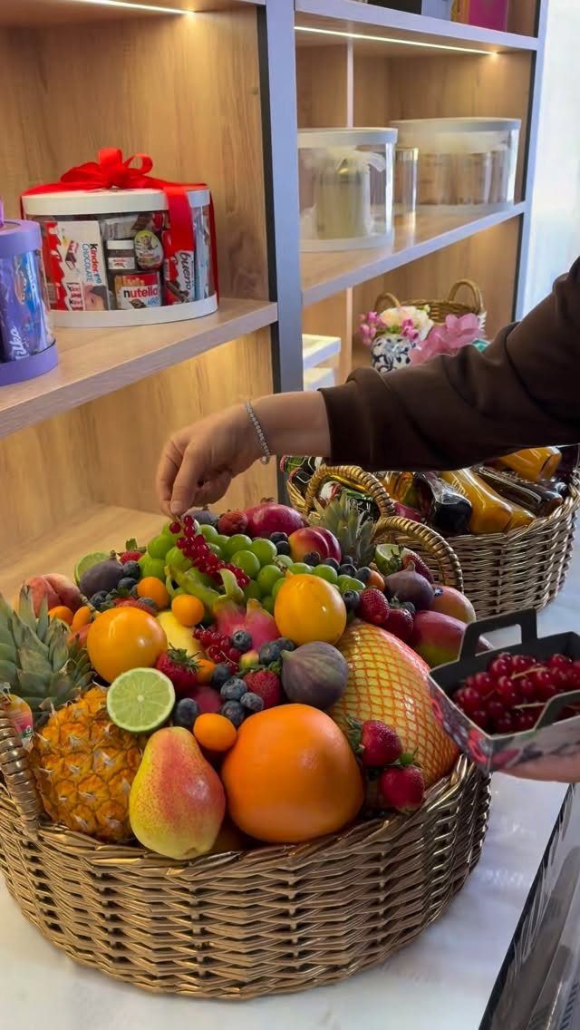 Wicker basket overflowing with colorful fresh fruits being arranged by a hand