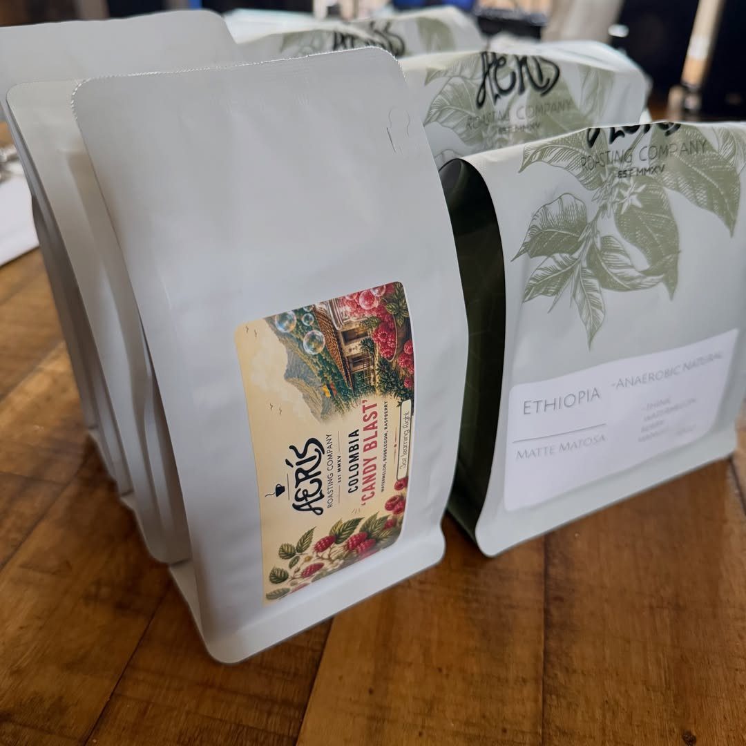 Coffee bean bags with colorful labels standing on a rustic wooden table.