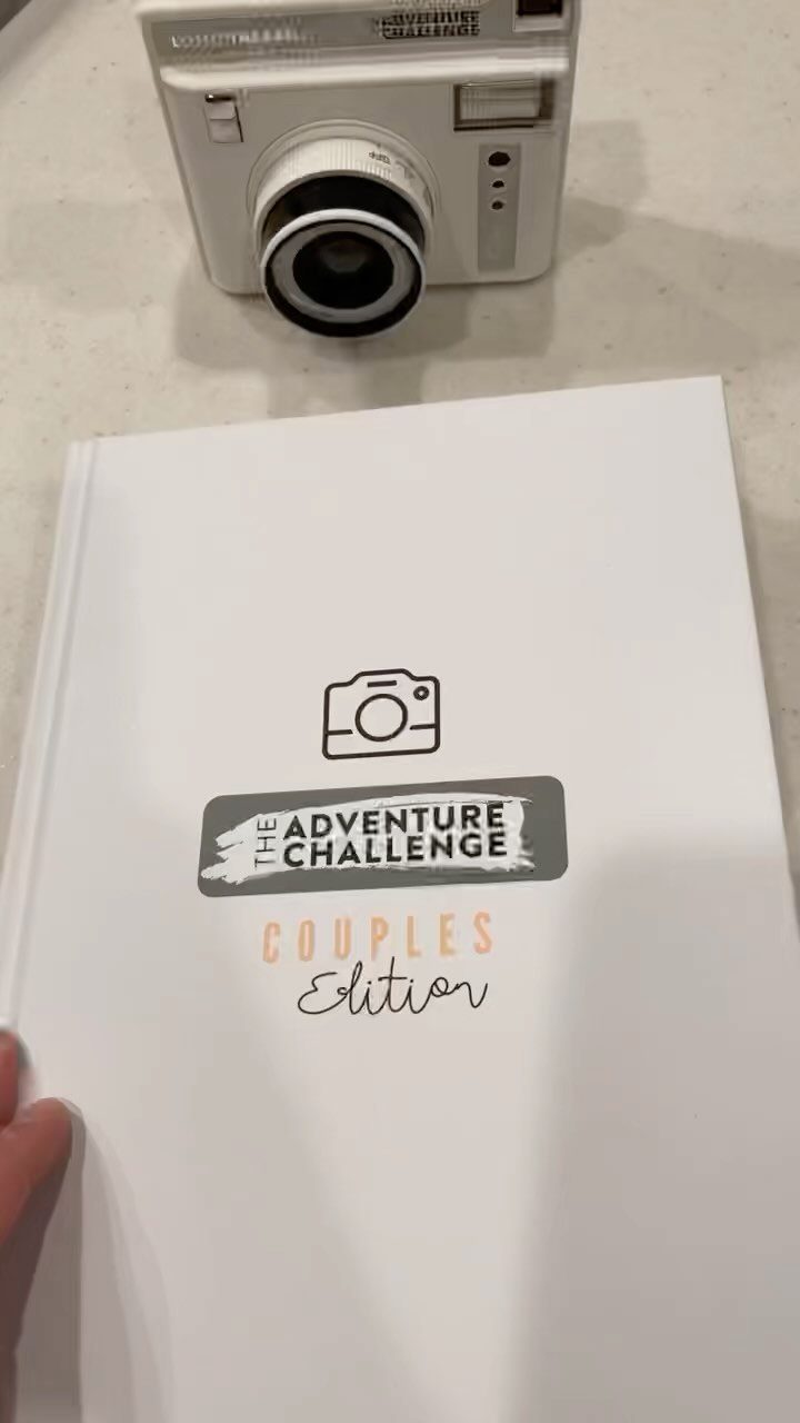 The Adventure Challenge Couples Edition book next to a white instant camera.